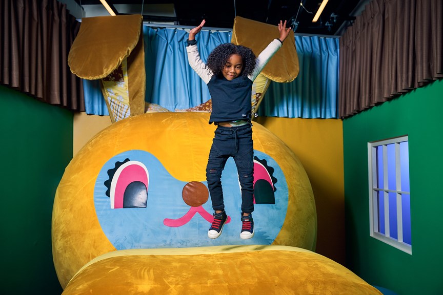  a young child jumps up in joy atop a giant stuffed bunny. 