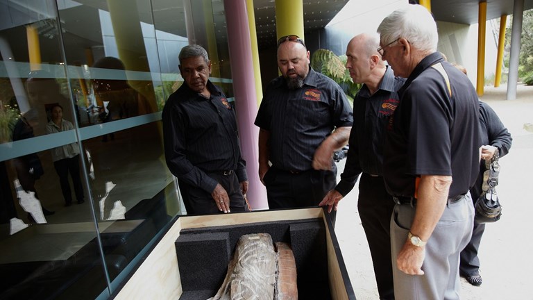 Group of four men looking into a box with a carving in it.