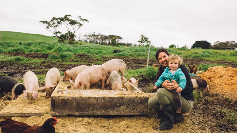 A farmer nurses her toddler amid a paddock of chickens and pigs.