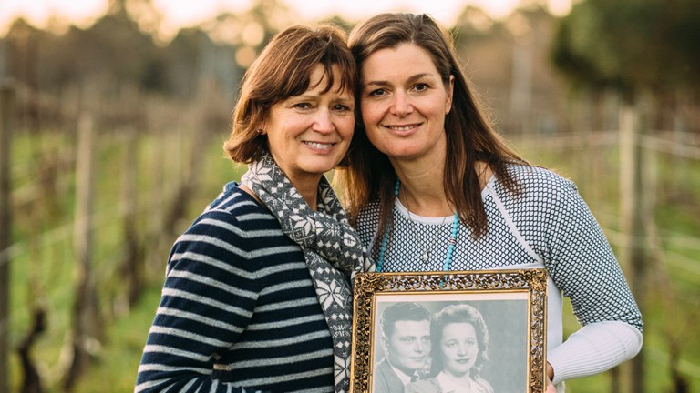 Two women in a vineyard holding a black and white photo.