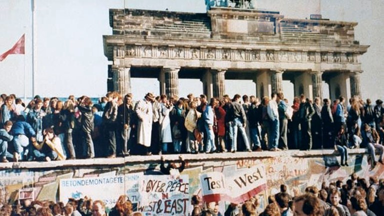 A crowd of people on top of a wall with a gate of stone columns behind them.
