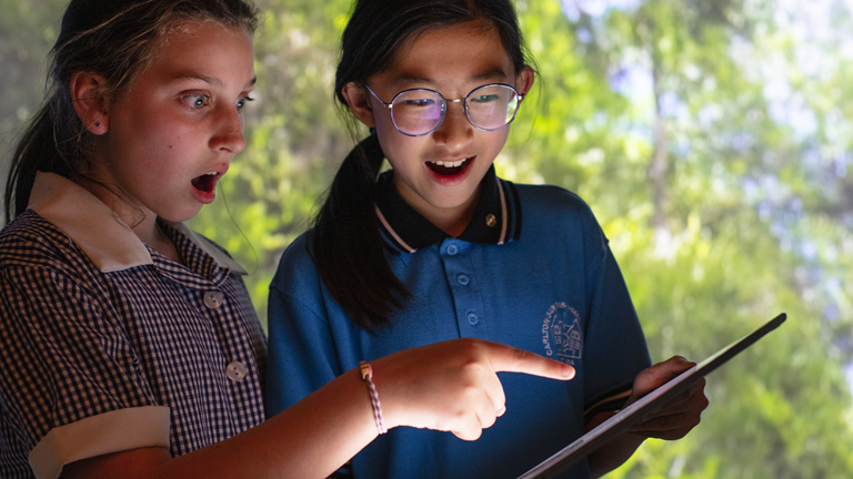 Two primary school students looking at computer tablet with Learning Lab projection in the background.